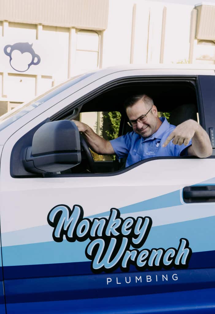 Wes, Master Plumber at Monkey Wrench Plumbing Sewer, and Drain andCo-Owner of Monkey Wrench, pointing to the company logo on his F-150 truck