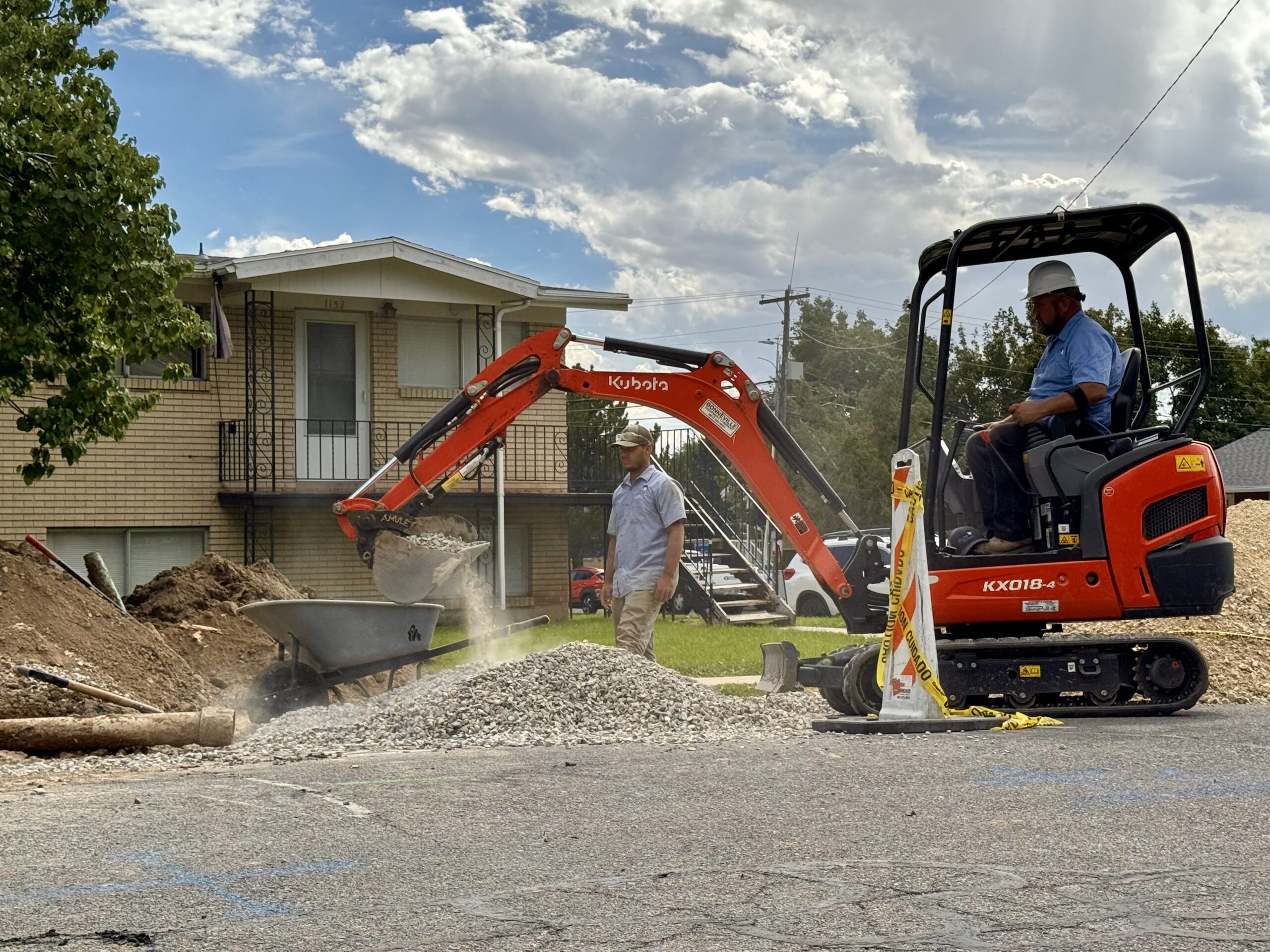 Excavator placing gravel bedding beside an open sewer trench in Provo, Utah