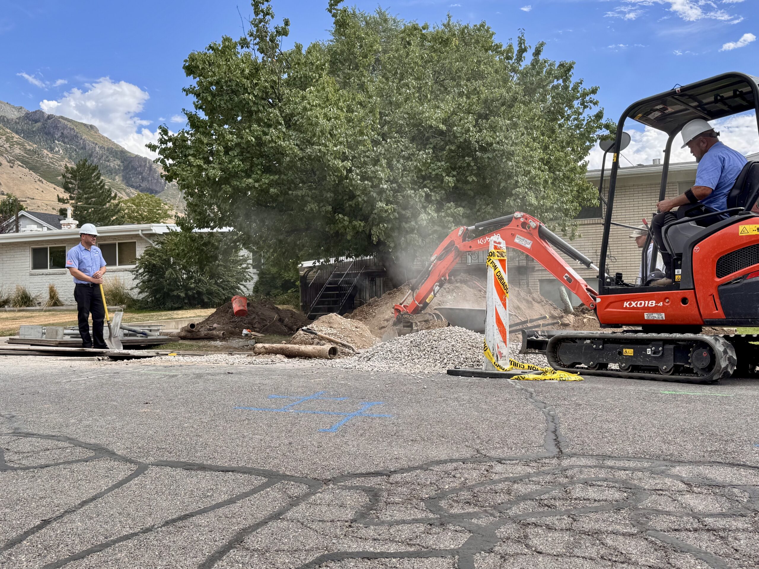 Kubota mini excavator digging a sewer line trench outside a mid-century Provo home